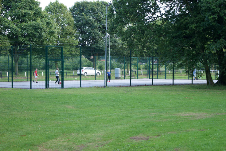 A group of children playing football in a multi-use games area.